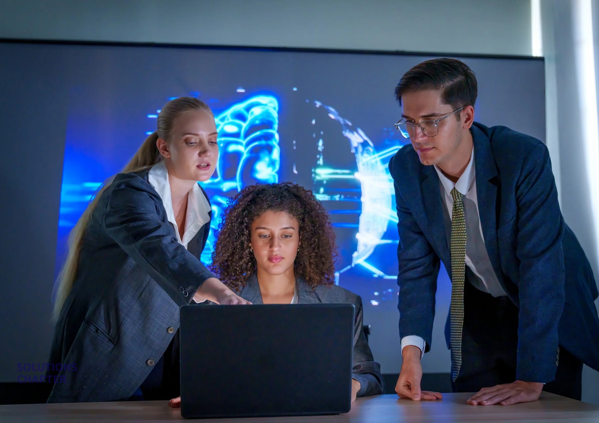 Three business professionals collaborating around a laptop, analyzing digital data on a screen, representing teamwork, data-driven decision-making, and modern business strategy.
